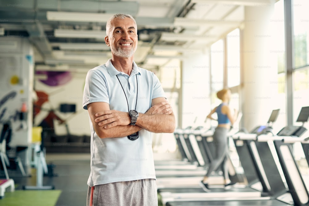 Portrait of confident mature fitness coach standing with crossed arms in a gym and looking at camera.