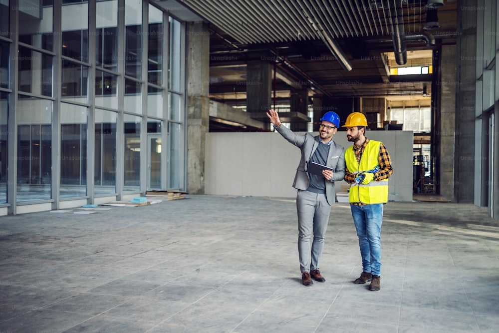 Architect holding tablet and talking with construction worker about new ideas on project they working on. Building in construction process interior.