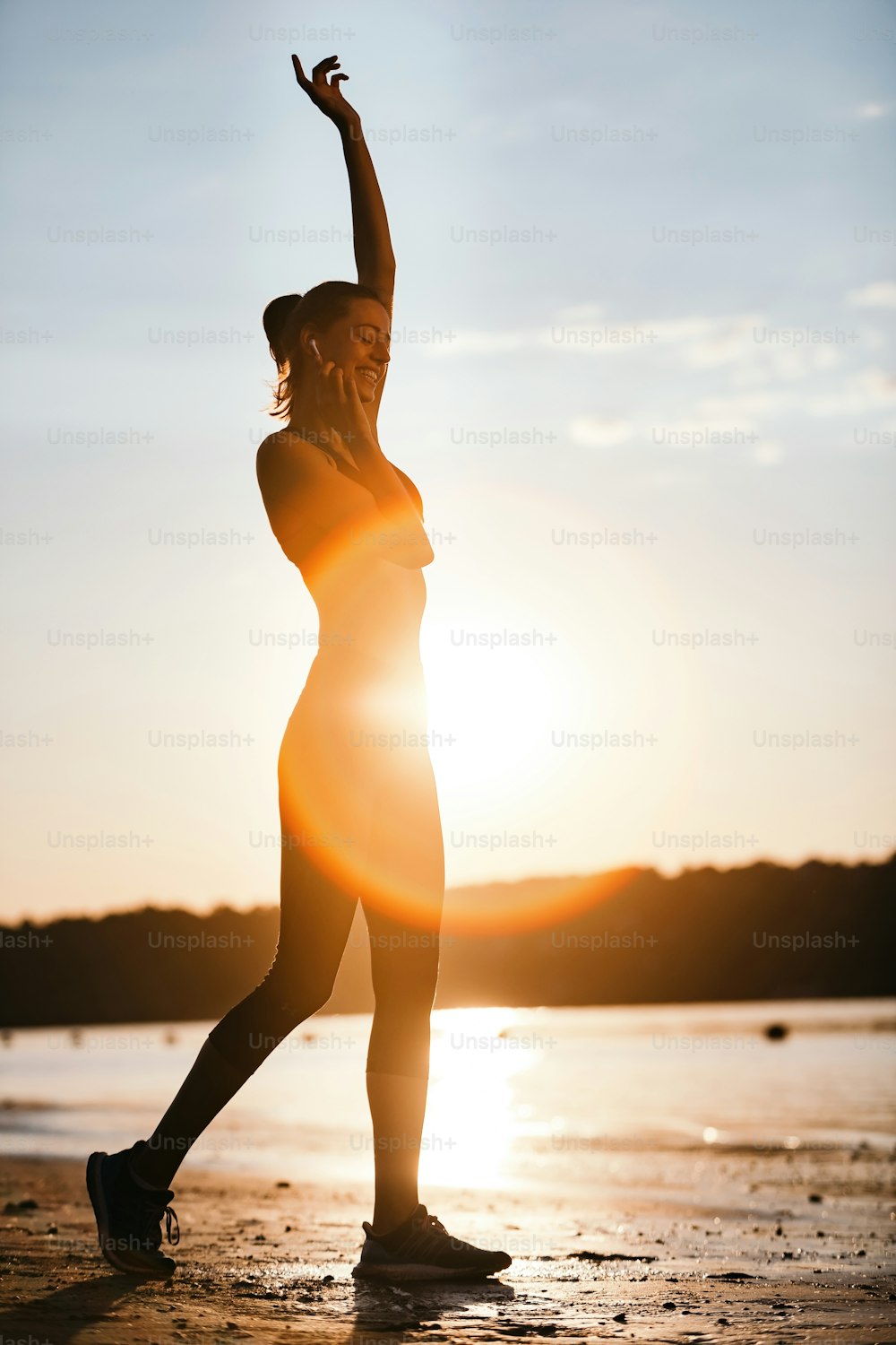 日の出に川辺で運動しながらイヤホンで音楽を聴く幸せな運動女性。