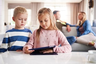 Niños enfocados en el uso de la tecnología y padres en segundo plano