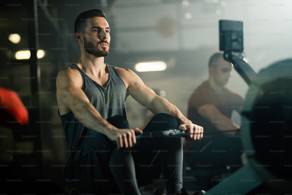 Homem de construção muscular usando máquina de remo enquanto se exercita em uma academia.