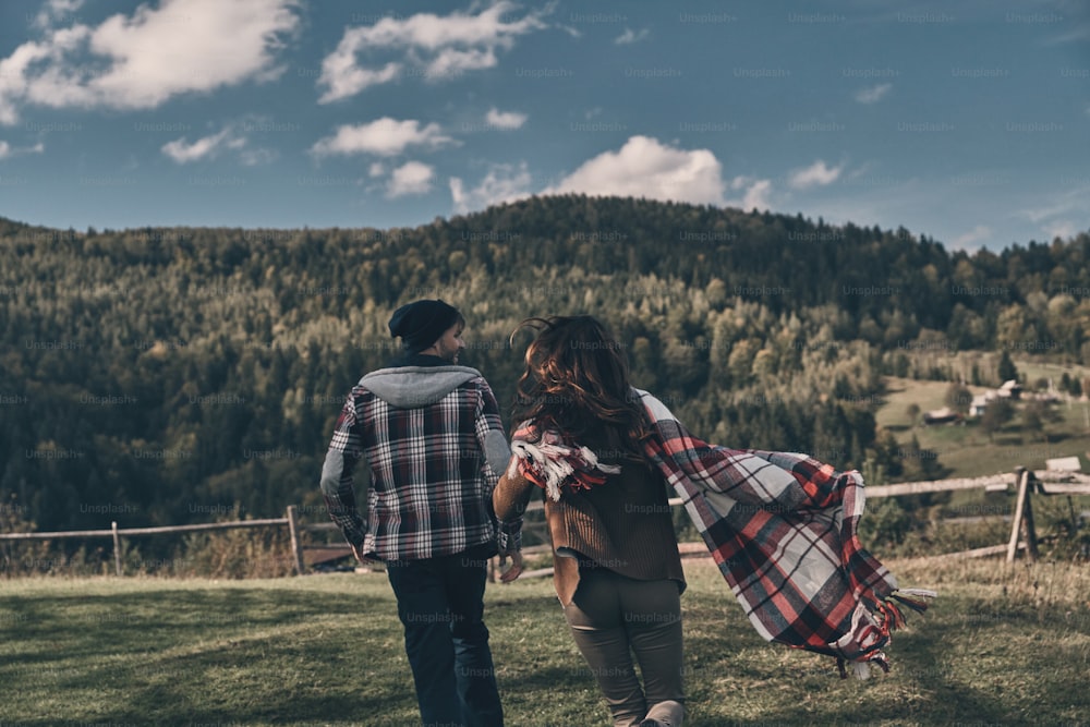 Vista trasera de una joven pareja juguetona que corre mientras pasa el tiempo despreocupado en el valle en las montañas