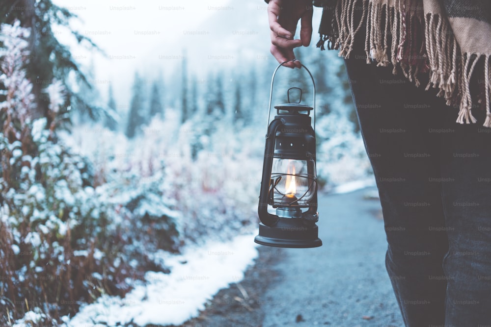 Frau, die mit Öllampe durch verschneite Wälder reist. Nahaufnahme. Poncho tragen. Der Winter kommt. Fernweh und Boho-Stil