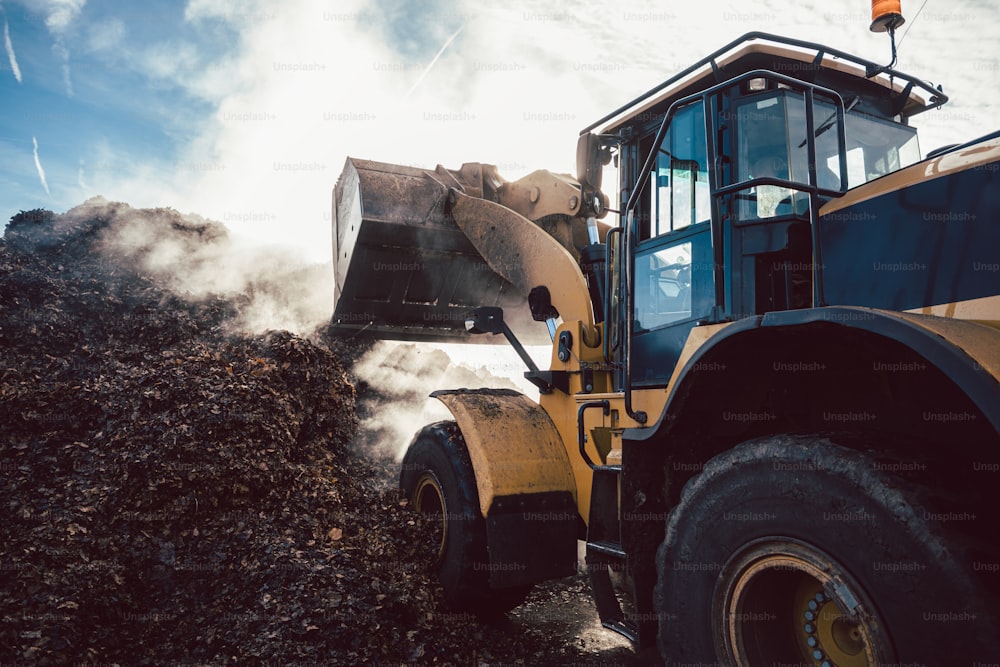Earth mover working on pile of compost in industrial facility