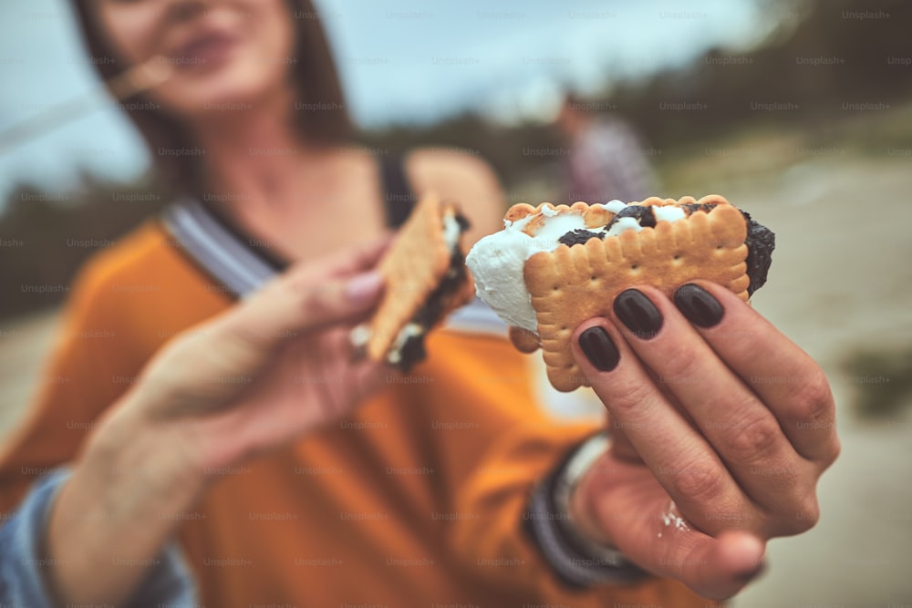 Hora de la merienda. Primer plano de la mano femenina de la sonrisa sosteniendo la galleta de chocolate rellena dulce con su amiga