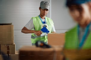 African American woman taping carboard boxes while working at distribution warehouse.