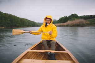 Girl in yellow raincoat paddling the canoe. Paddling boat in the rain.