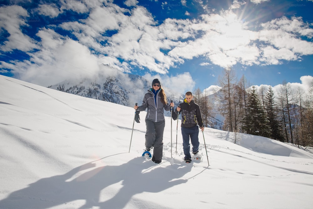 Jovem casal faz caminhadas com raquetes de neve nas montanhas.