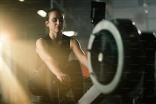 Jovem esportista que se exercita na máquina de remo durante o treinamento esportivo em uma academia.