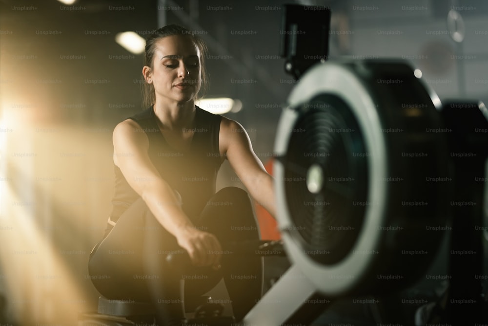 Young sportswoman exercising on rowing machine during sports training in a gym.