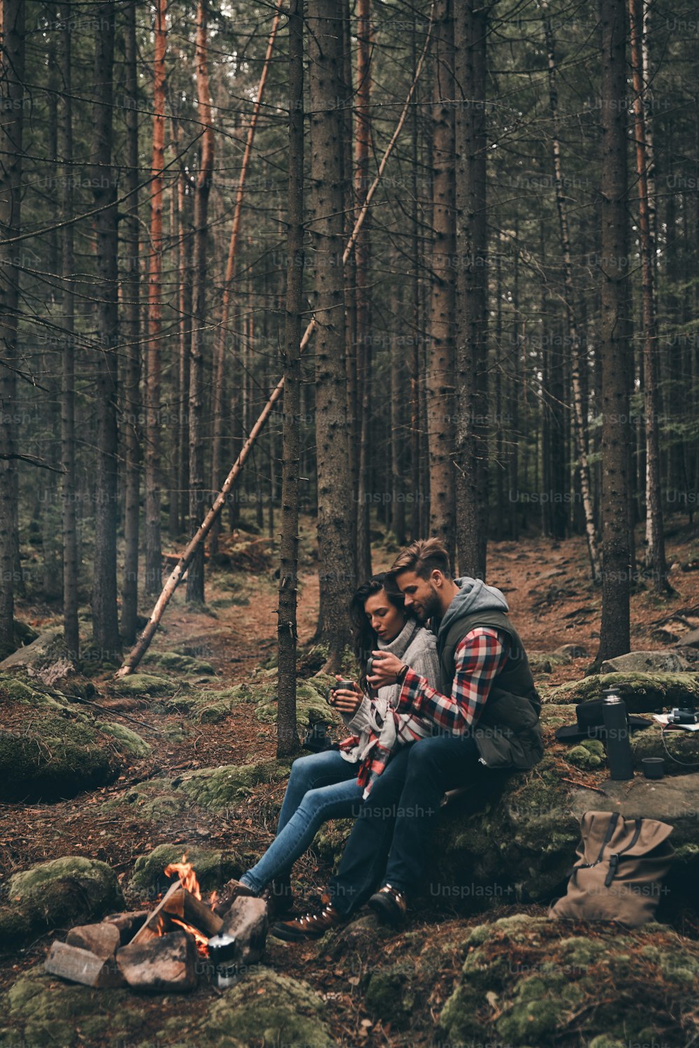 Beautiful young couple holding cups while warming up near the campfire