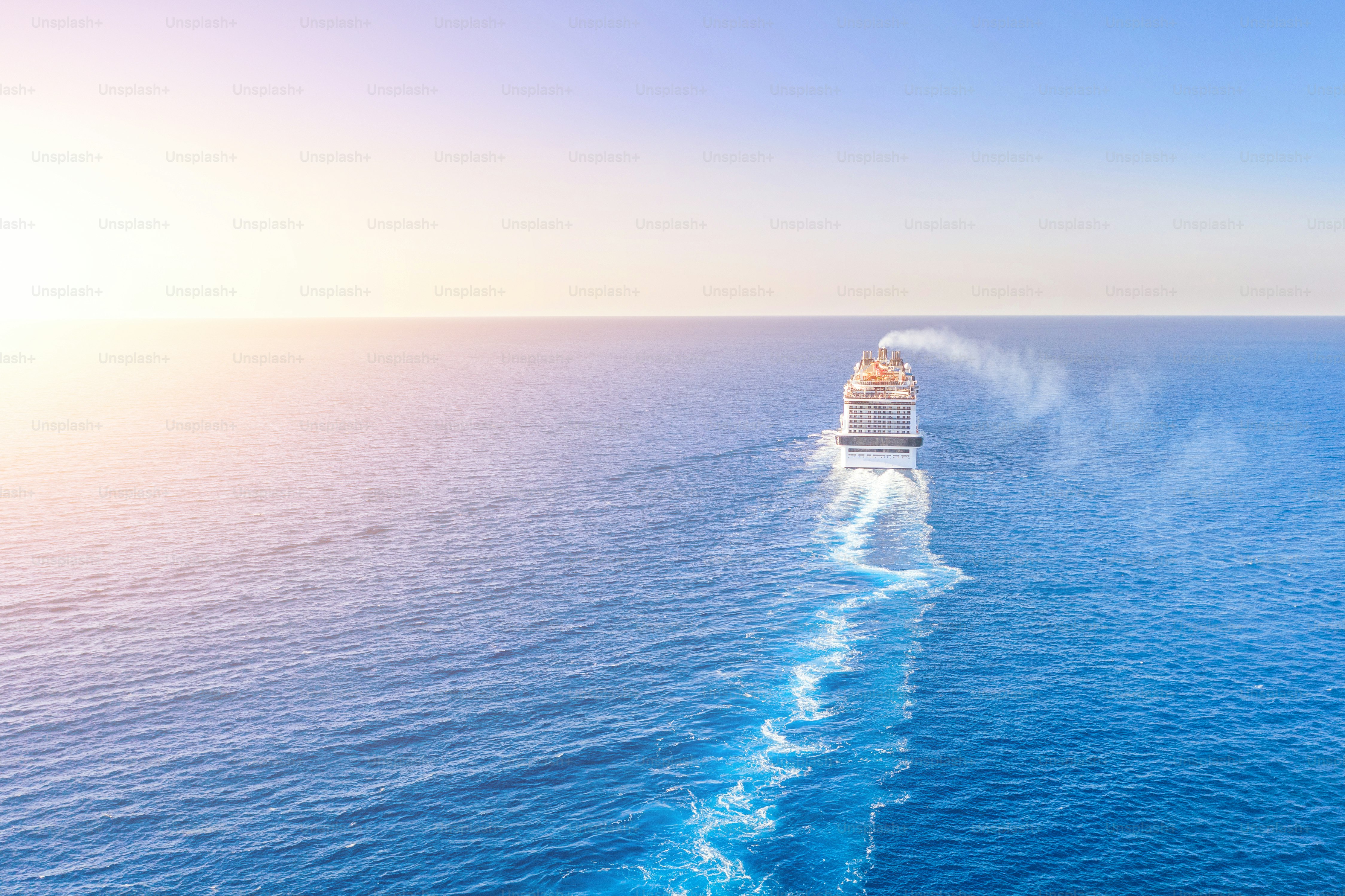 Cruise ship liner goes into horizon the blue sea leaving a plume on the surface of the water seascape during sunset. Aerial view, concept of sea travel, cruises