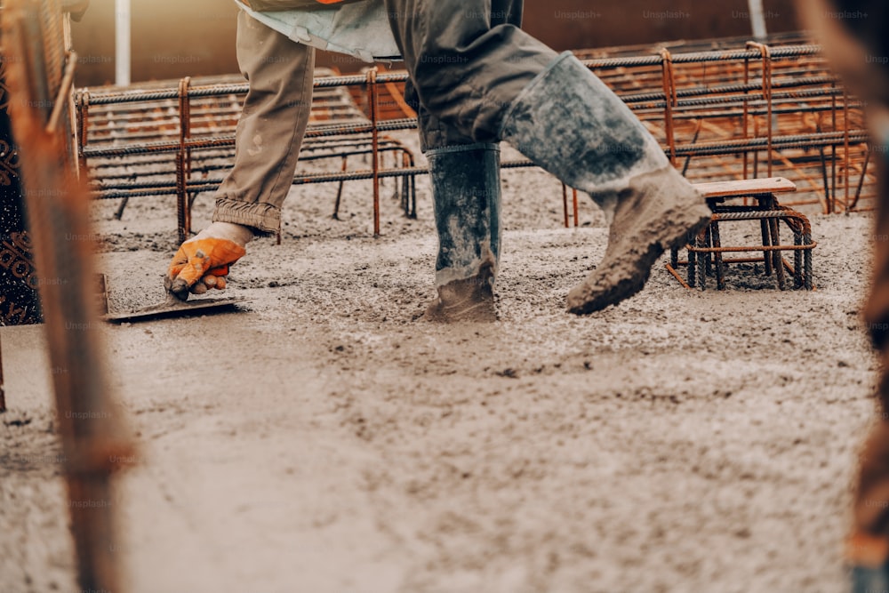 Construction site worker in boots and uniform finishing concrete on ground.