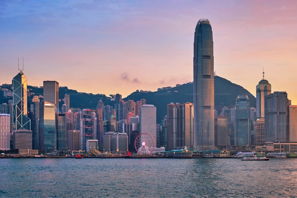 Hong Kong skyline cityscape downtown skyscrapers over Victoria Harbour in the evening with junk tourist ferry boat on sunset with dramatic sky. Hong Kong, China