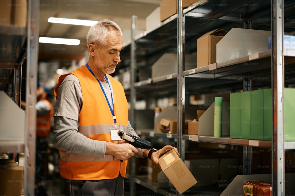 Mature warehouse worker scanning packages at storage compartment.