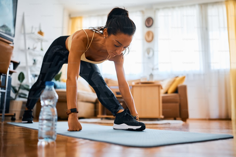 Athletic woman stretching while warming up for sports training at home.