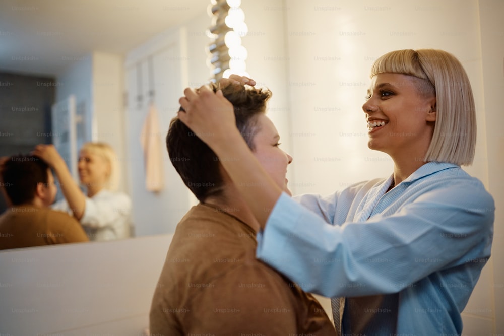 Lesbienne heureuse ajustant la coiffure de sa copine dans la salle de bain.