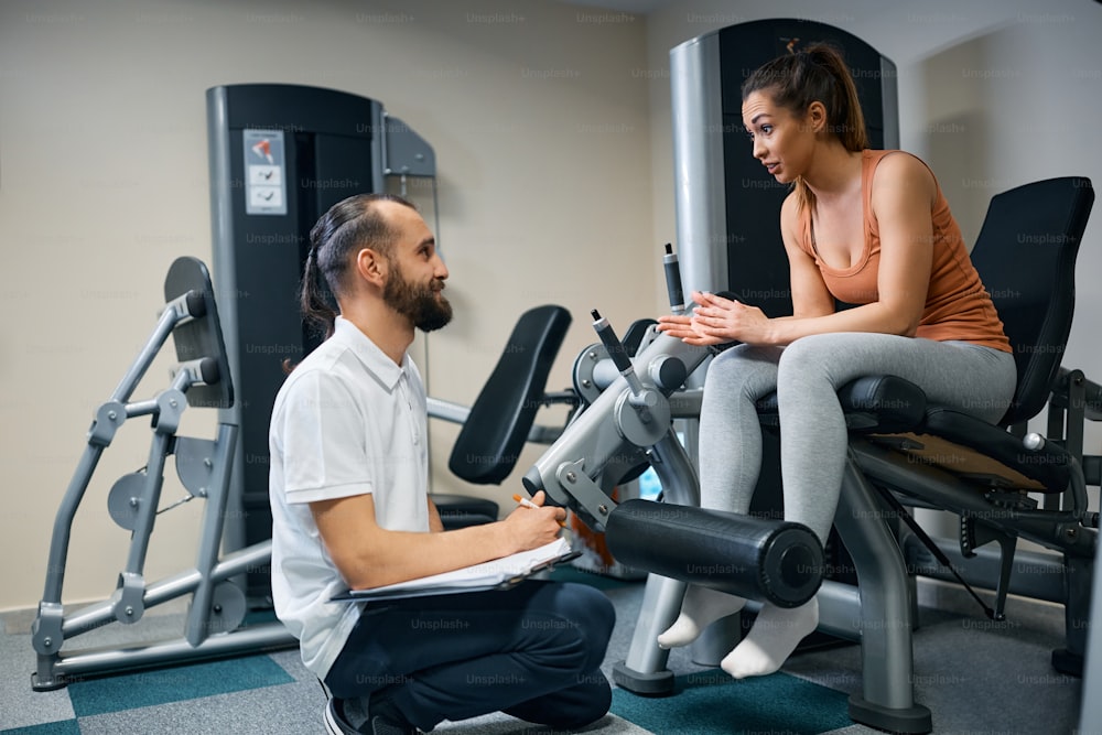 Fisioterapista che prende appunti mentre parla con una donna atletica dei suoi futuri piani di allenamento nel centro benessere.