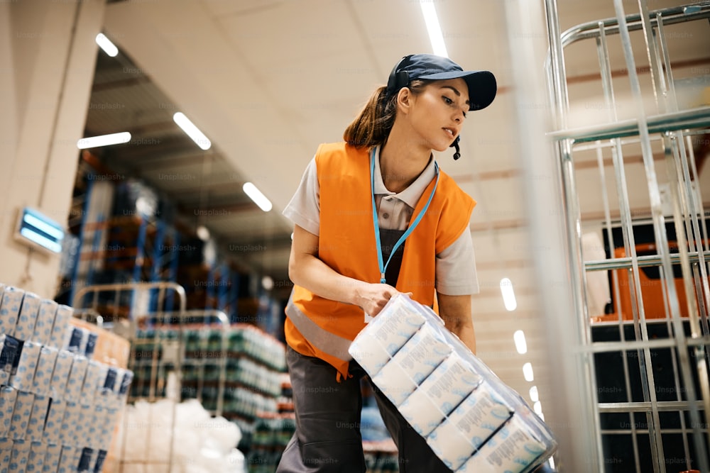 Young female worker stacking packages on moving rack while working at distribution warehouse.
