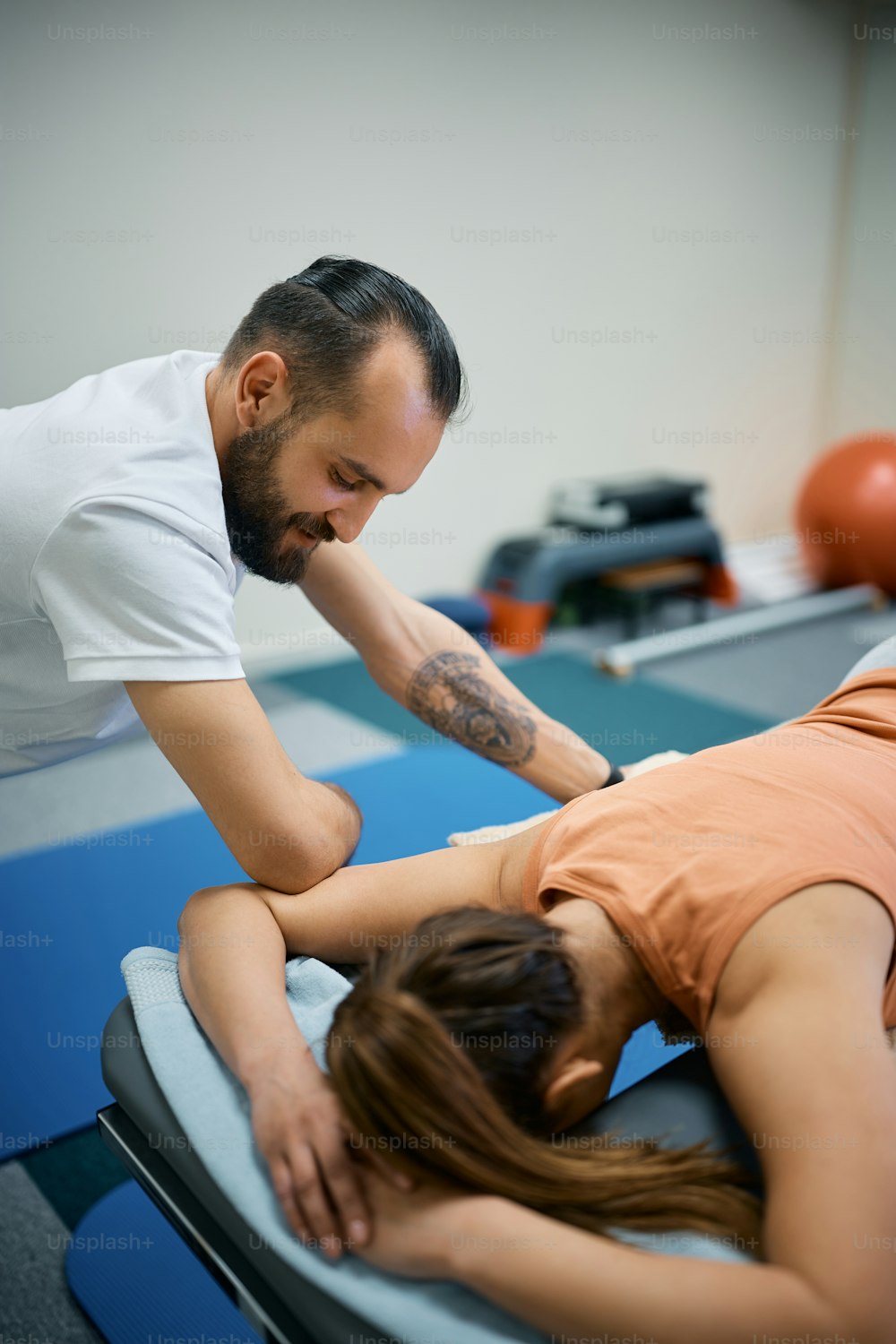 Male physical therapist giving sports massage to a woman at health club.