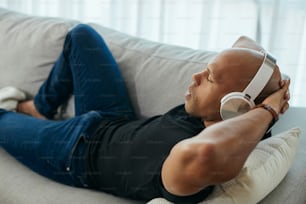 Relaxed black man listening music with eyes closed on the sofa at home.