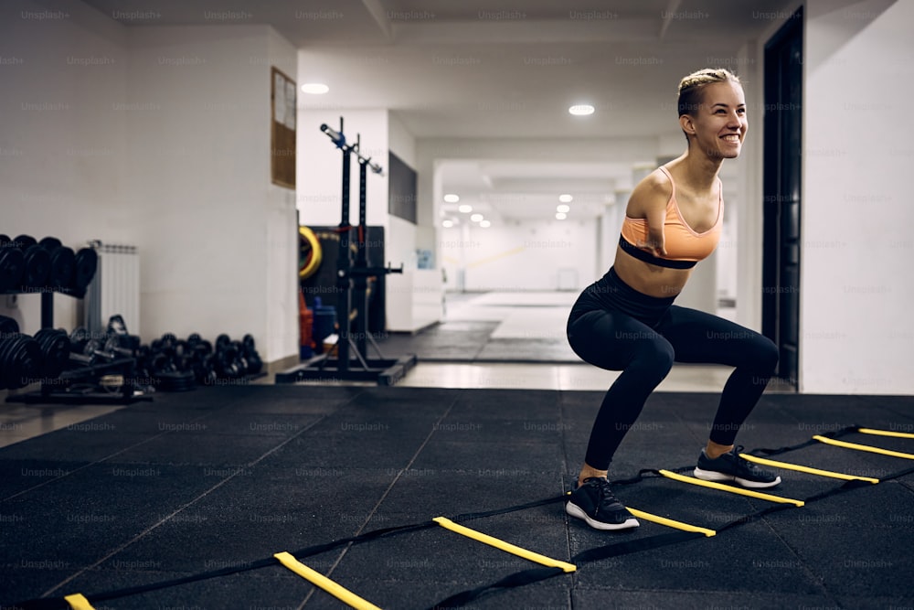Femme athlétique heureuse avec un handicap utilisant l’échelle d’agilité des pieds lors d’un entraînement sportif dans un gymnase.