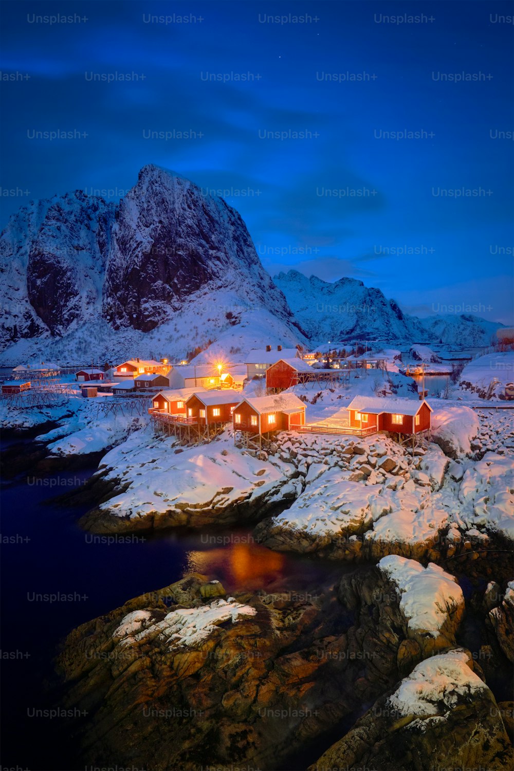 Famous tourist attraction Hamnoy fishing village on Lofoten Islands, Norway with red rorbu houses in winter snow illuminated in the evening