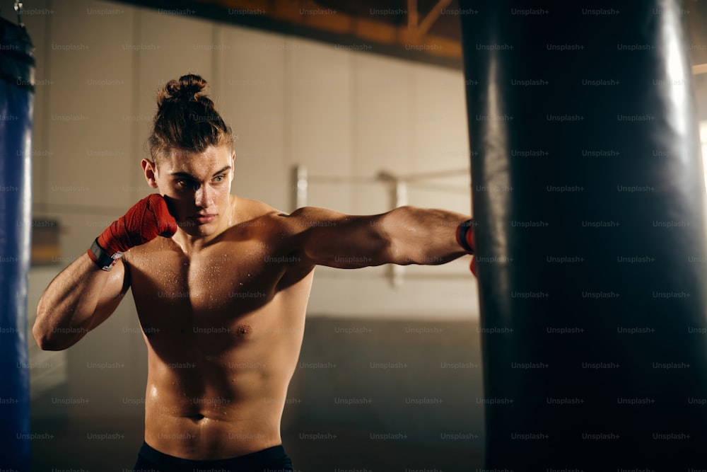 Jeune athlète frappant un sac de frappe lors d’un entraînement de boxe dans un club de boxe.