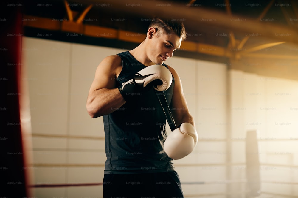 Jeunes boxeurs se préparant à l’entraînement sportif et ajustant ses gants sur le ring de boxe.