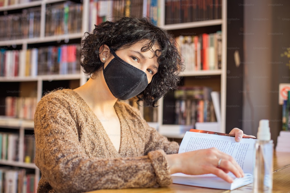 Woman with anti virus mask in library reading book.