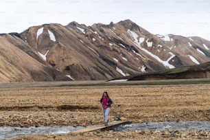 Traveler hiking at Landmannalaugar surreal nature landscape in highland of Iceland, Nordic, Europe. Beautiful colorful snow mountain terrain famous for summer trekking adventure and outdoor walking.