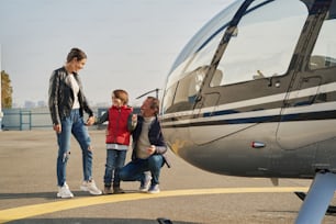 Excited little boy and his parents smiling while posing near a bright new aircraft