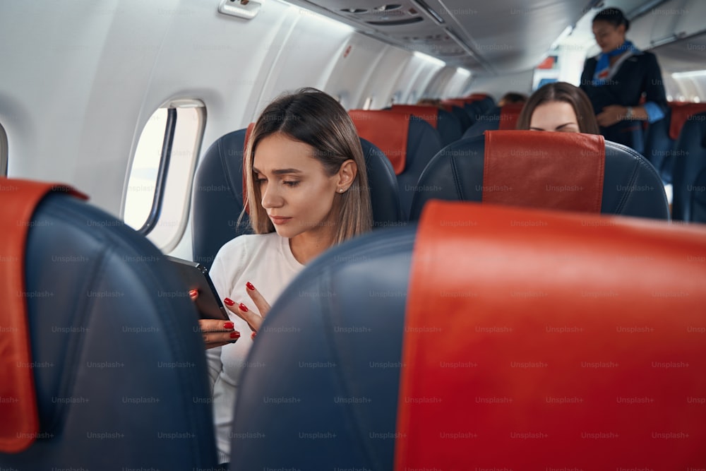 Donna caucasica in aeroplano che si siede vicino alla finestra e usa il suo telefono cellulare