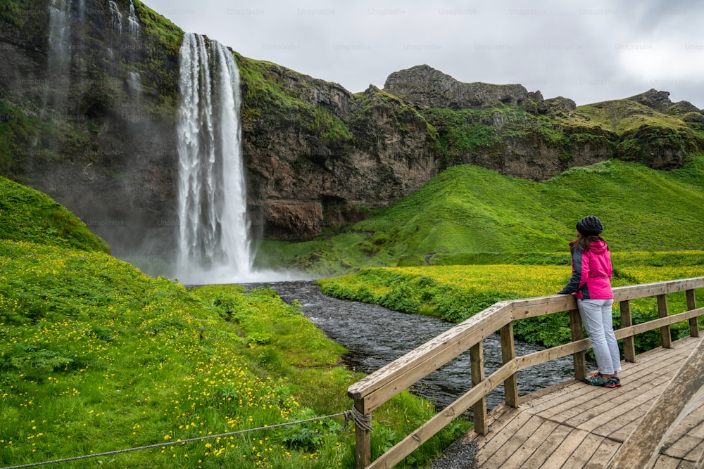 Mulher viajante na cachoeira mágica Seljalandsfoss na Islândia localizada perto do anel viário do sul da Islândia. Majestoso e pitoresco, é um dos lugares de tirar o fôlego mais fotografados do deserto da Islândia