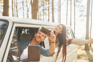 Making selfie. Young couple is traveling in the forest at daytime together.