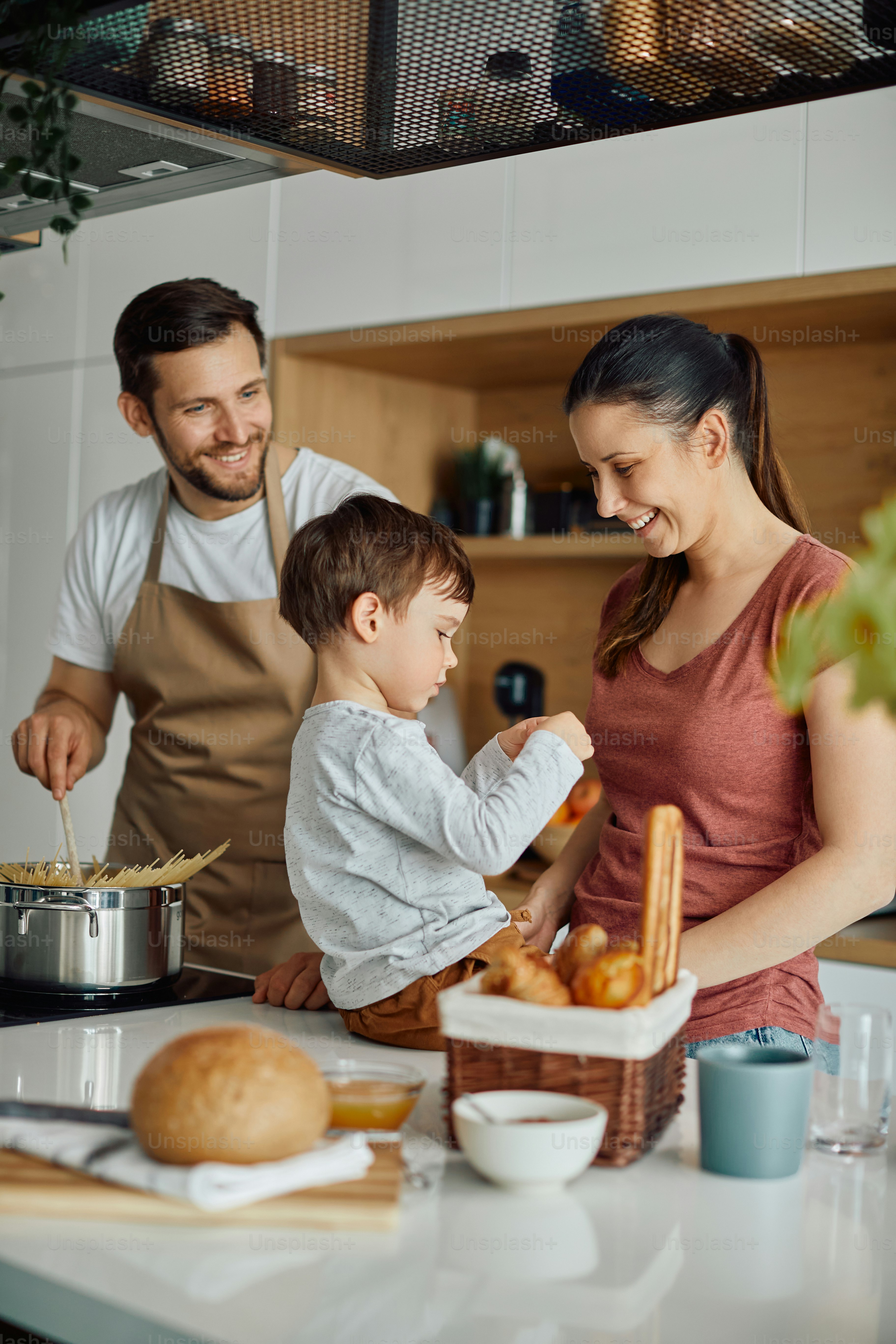 Des parents heureux qui s’amusent tout en préparant des repas avec leur petit garçon dans la cuisine.