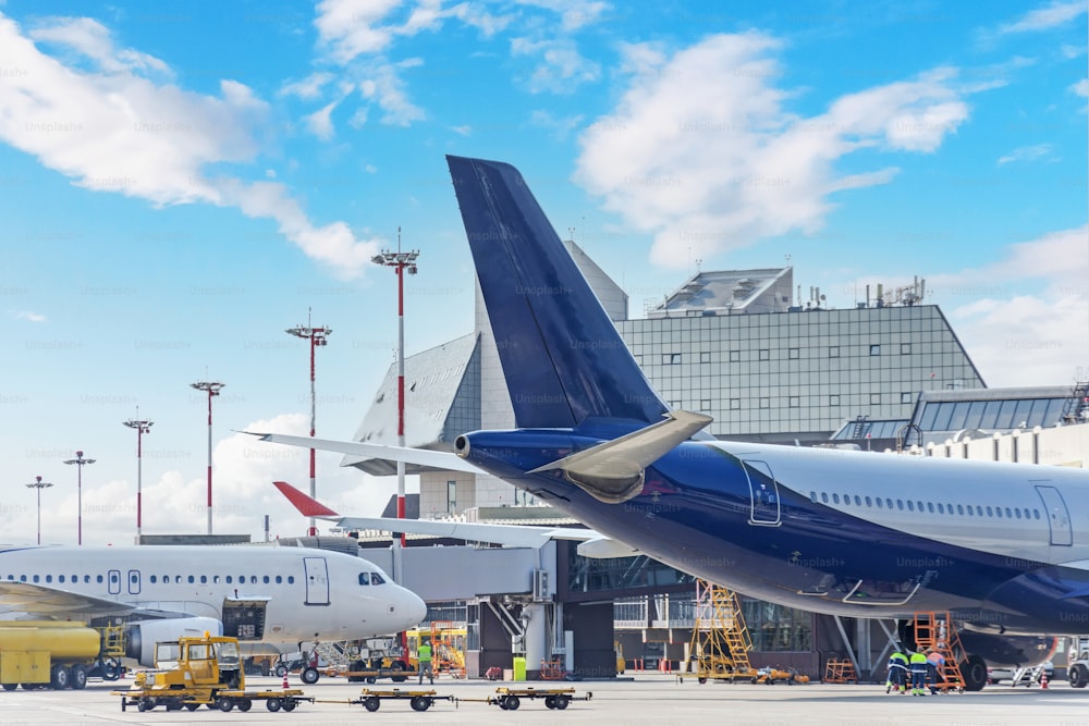 Aircraft in pre-flight maintenance and their tails at the airport next to the passenger terminal