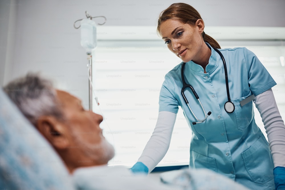 Smiling nurse taking care of mature patient who is recovering at the hospital ward.