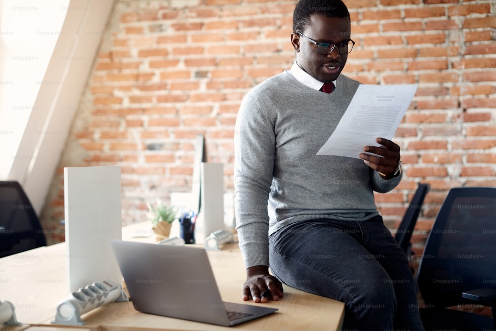 Empresário afro-americano analisando documentos enquanto está sentado em sua mesa de escritório.