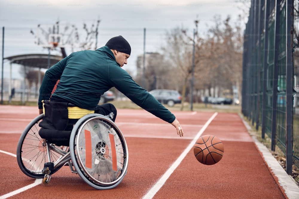 Männlicher Athlet im Rollstuhl beim Basketballtraining auf einem Außenplatz.