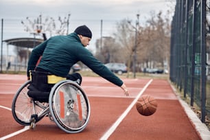 Male athlete in wheelchair practicing basketball on an outdoor court.
