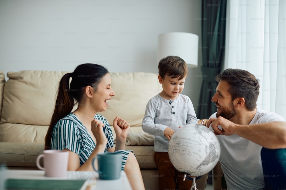 Happy parents teaching their small son about the globe at home.