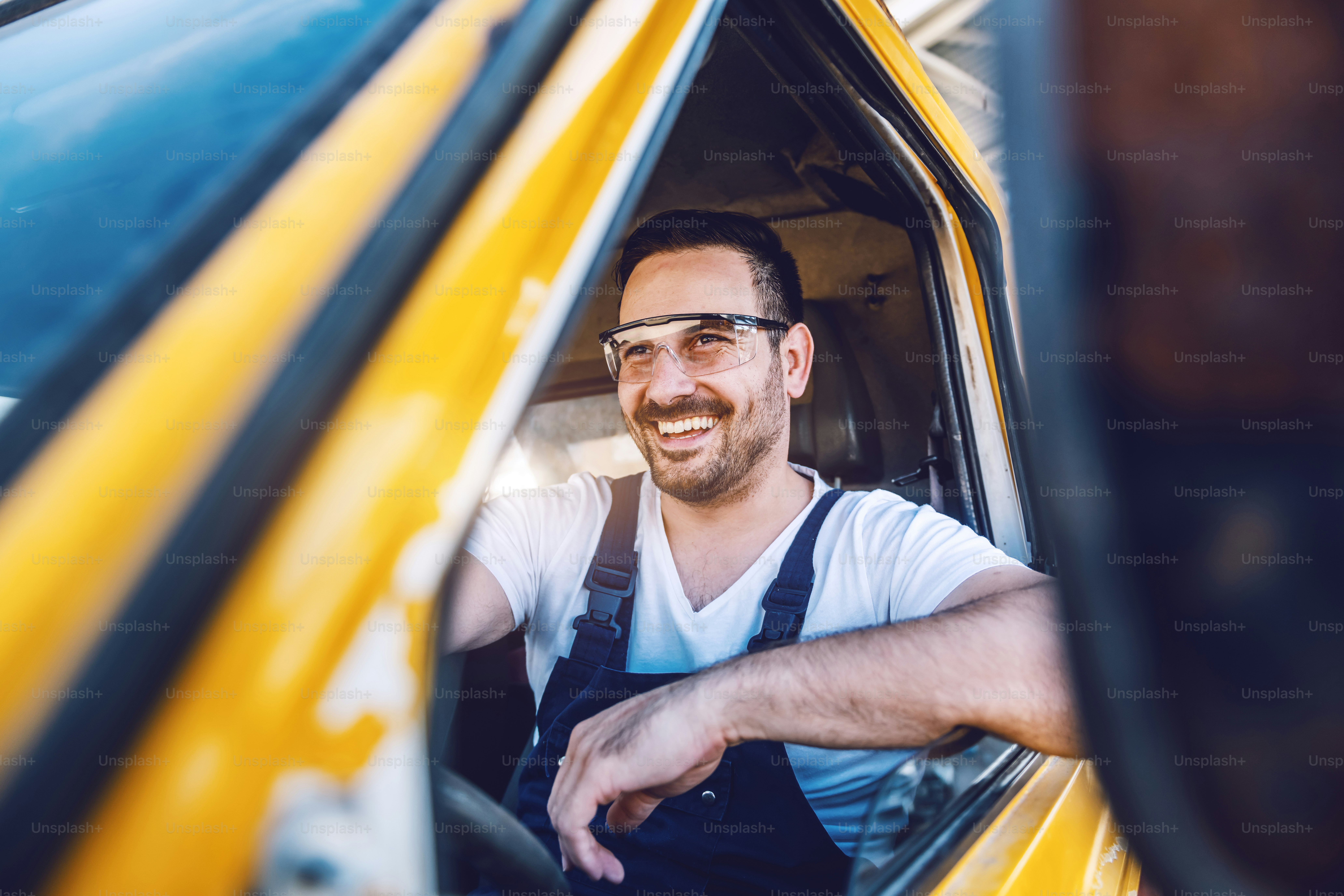 Smiling handsome unshaven worker driving vehicle on construction site ...