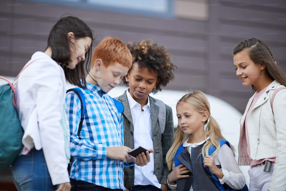 Gruppe von Klassenkameraden, die nach der Schule gemeinsam etwas auf dem Handy anschauen, während sie draußen stehen