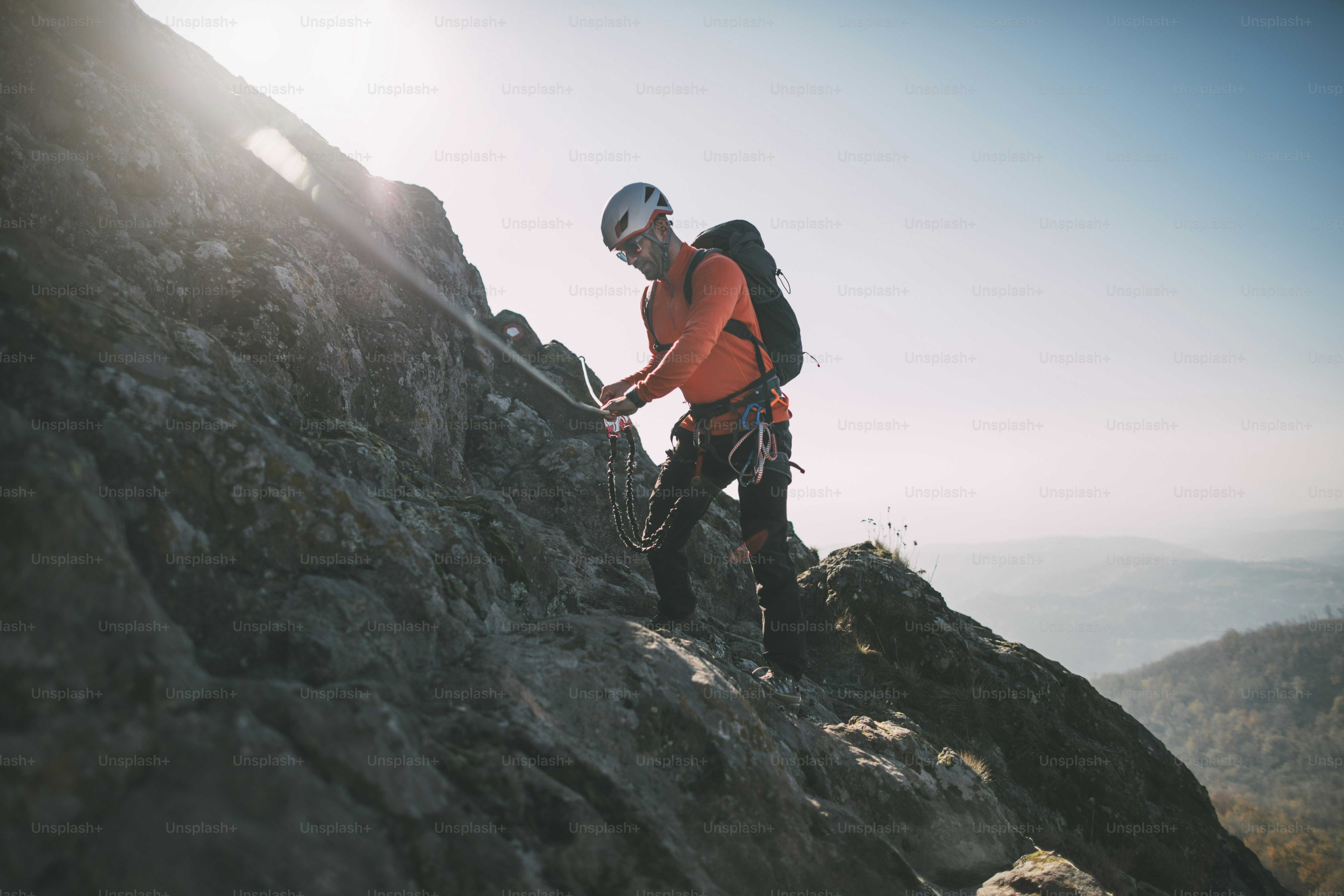 Mountaineer with backpack using climbing rope to climb rocky mountain summit. photo Adventure
