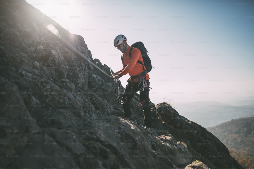 Alpinista con zaino che utilizza la corda da arrampicata per scalare la cima rocciosa della montagna.