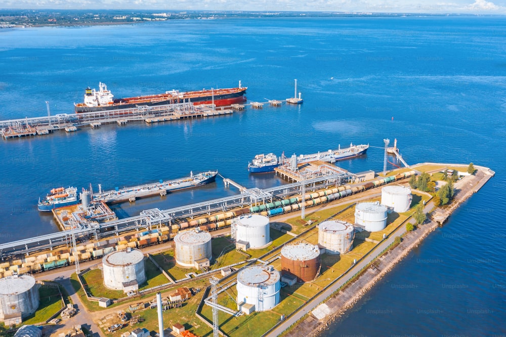 大型貯蔵タンクを備えた大型港湾石油積み込みターミナルの航空写真。輸送と配送のための船タンカーのポンプステーションを使用した海上バルク貨物の輸送のための鉄道インフラ
