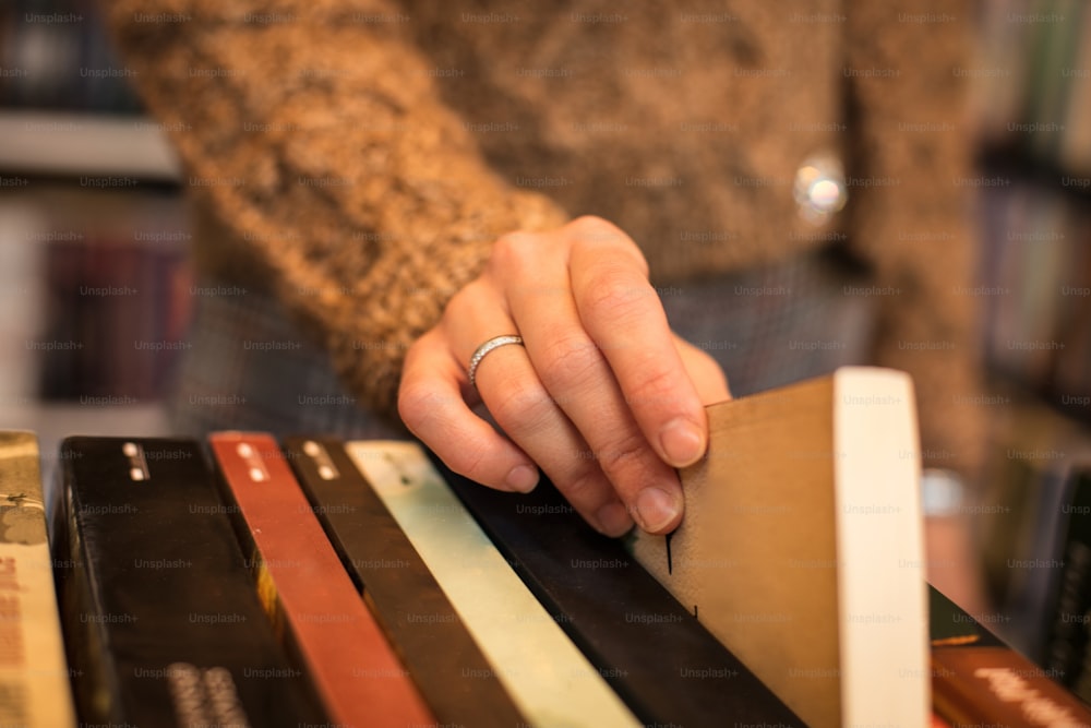 Woman in the library chooses a book. Focus is on hand. Close up.