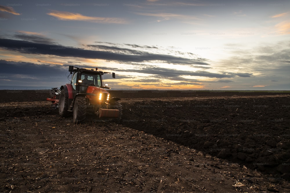 Traktor pflügt das Feld am Abend bei Sonnenuntergang.