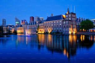 View of the Binnenhof House of Parliament and the Hofvijver lake with downtown skyscrapers in background illuminated in the evening. The Hague, Netherlands
